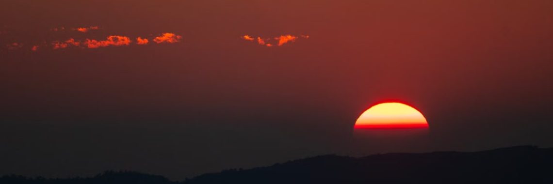 Captivating sunset with vibrant red hues over mountainous silhouette landscape.